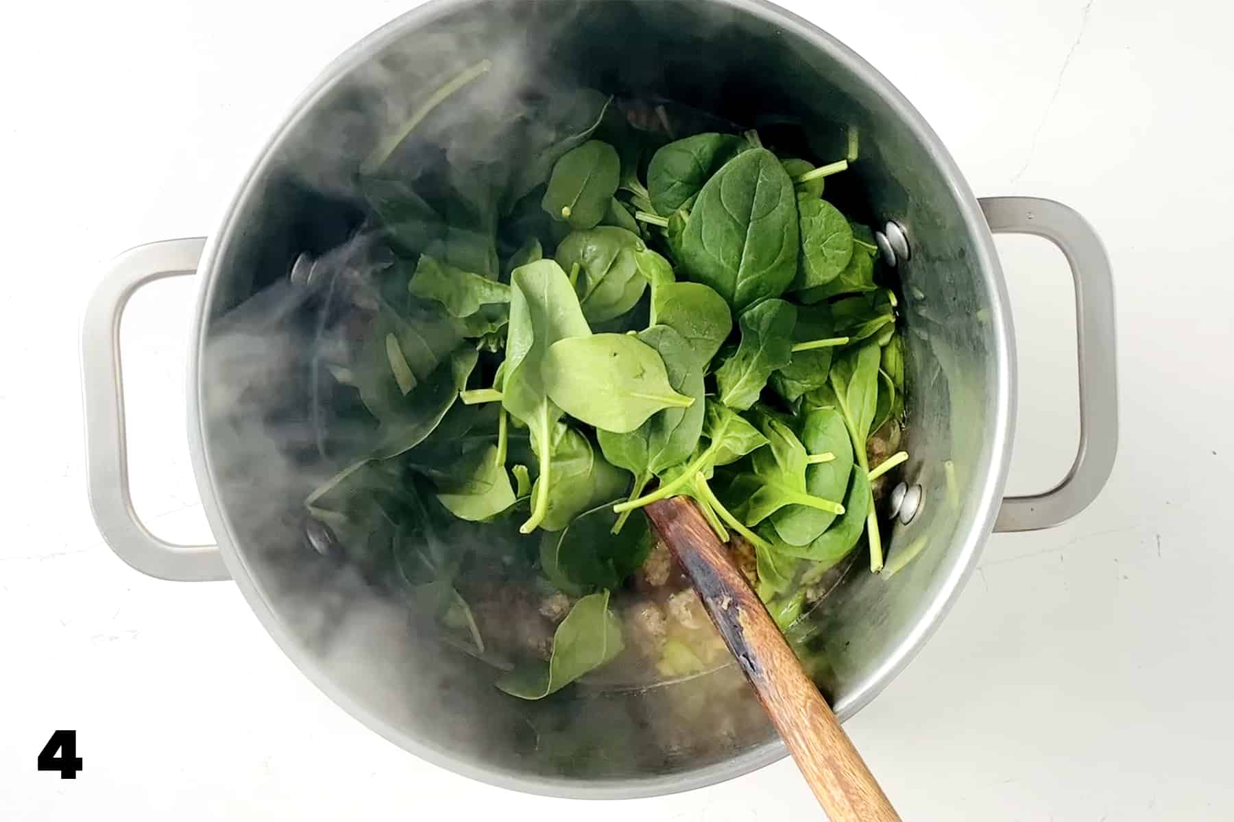 fresh spinach in stockpot with wooden spoon