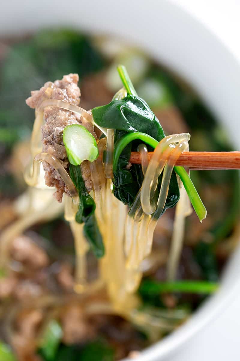 chopstick full of glass noodles, greens and ground pork
