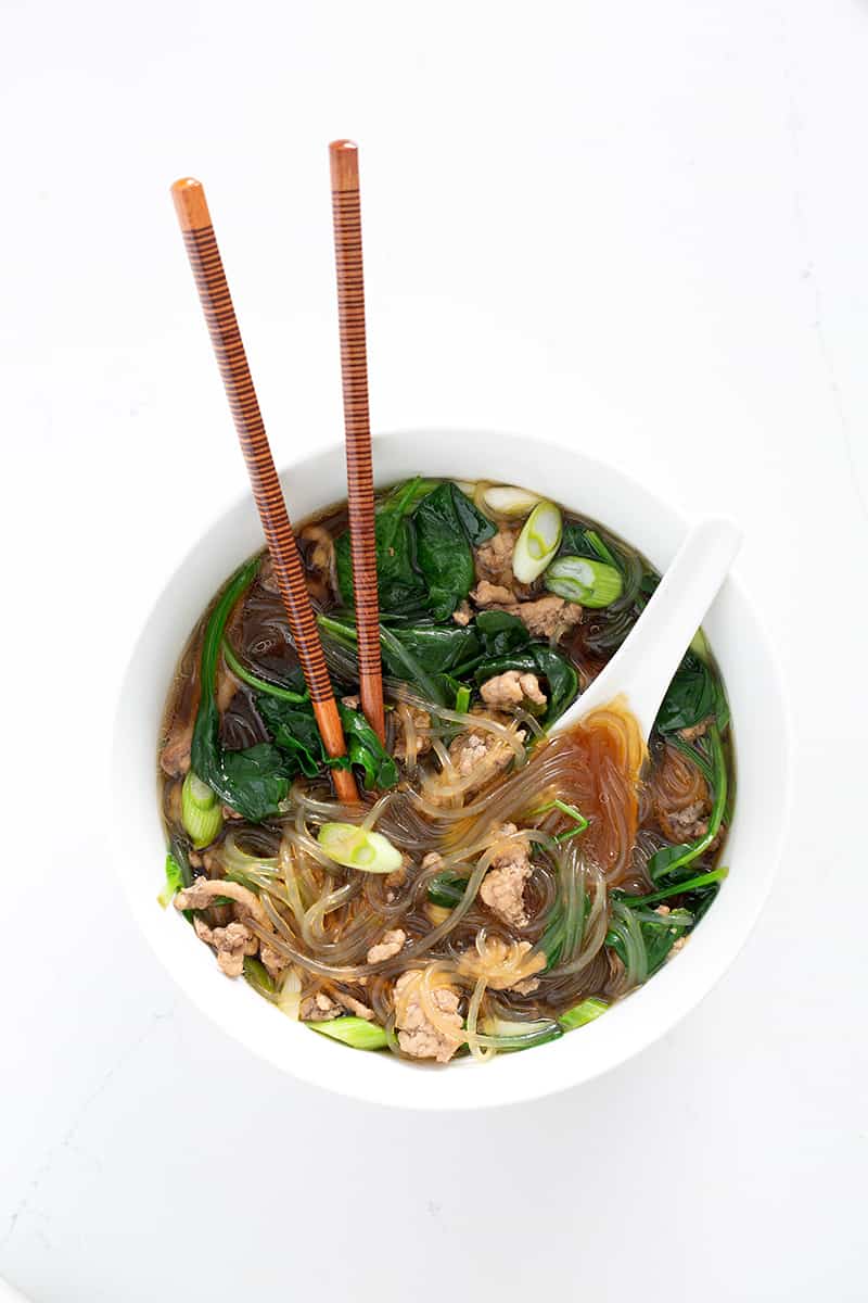 bowl of glass noodle soup, ceramic asian spoon and chopsticks on white