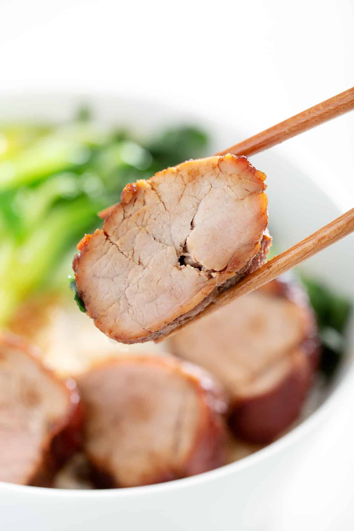 close of of chopsticks holding a char siu pork slice