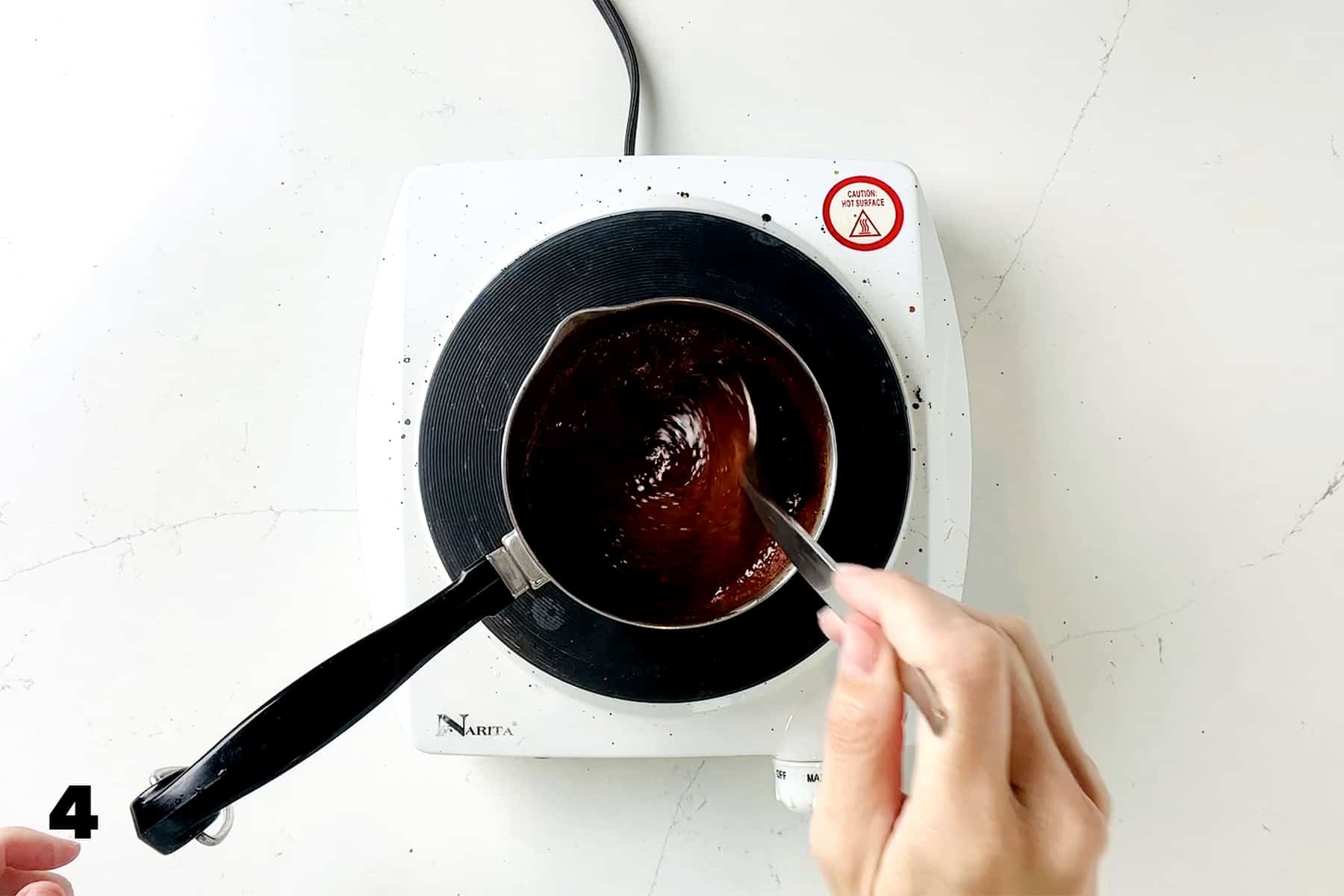 hand stirring char siu sauce in small pan over cooktop