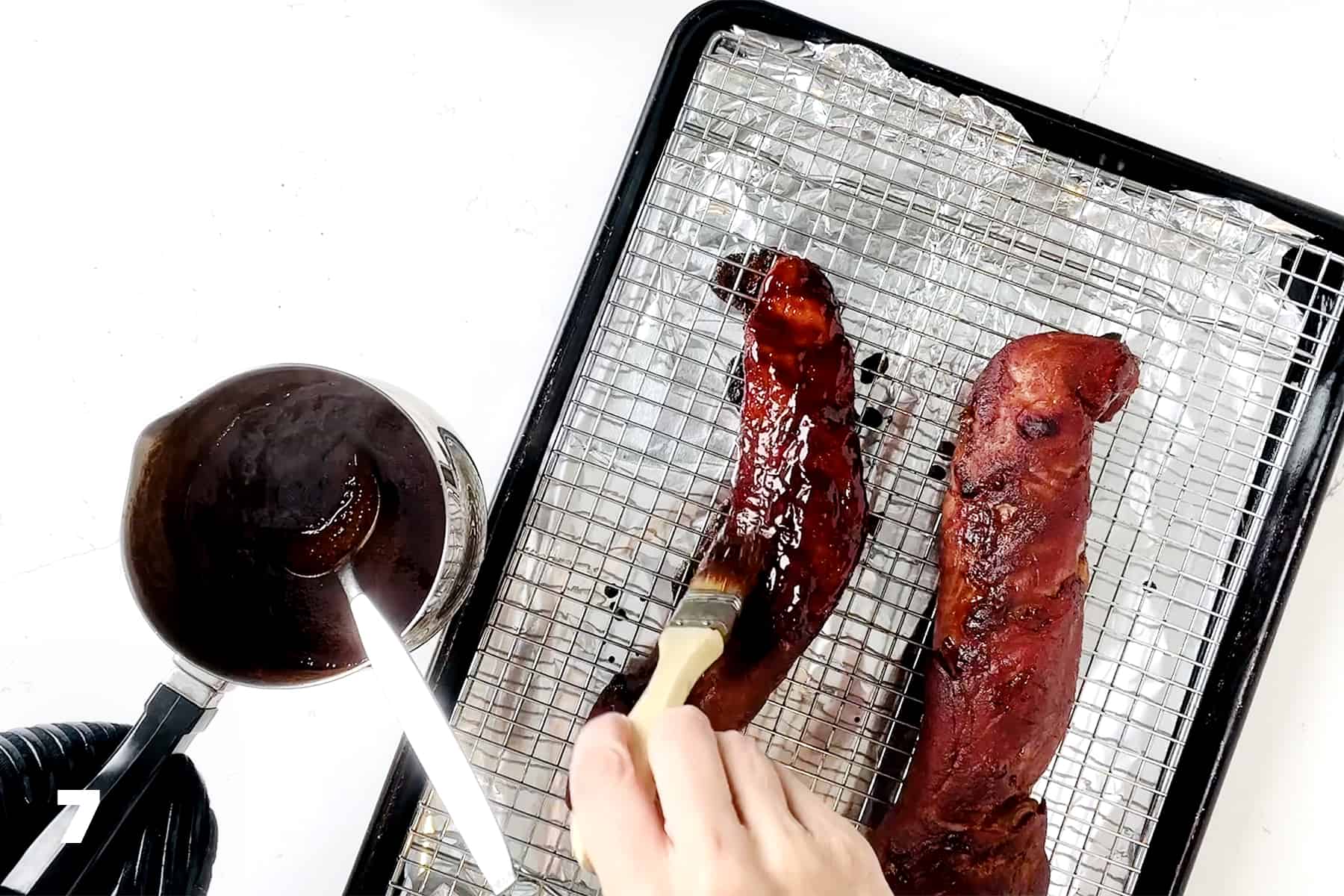 basting pork tenderloins with char siu glaze on foil lined baking sheet