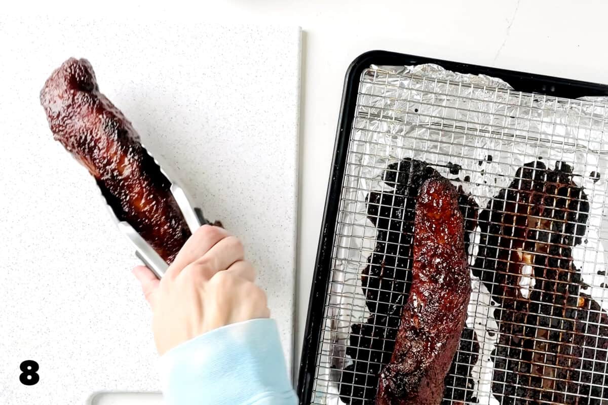 hands using tongs to place Chinese BBQ pork tenderloins on cutting board