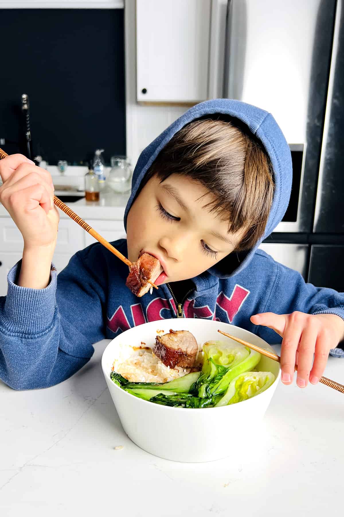 kid biting into sauce siu pork with chopsticks