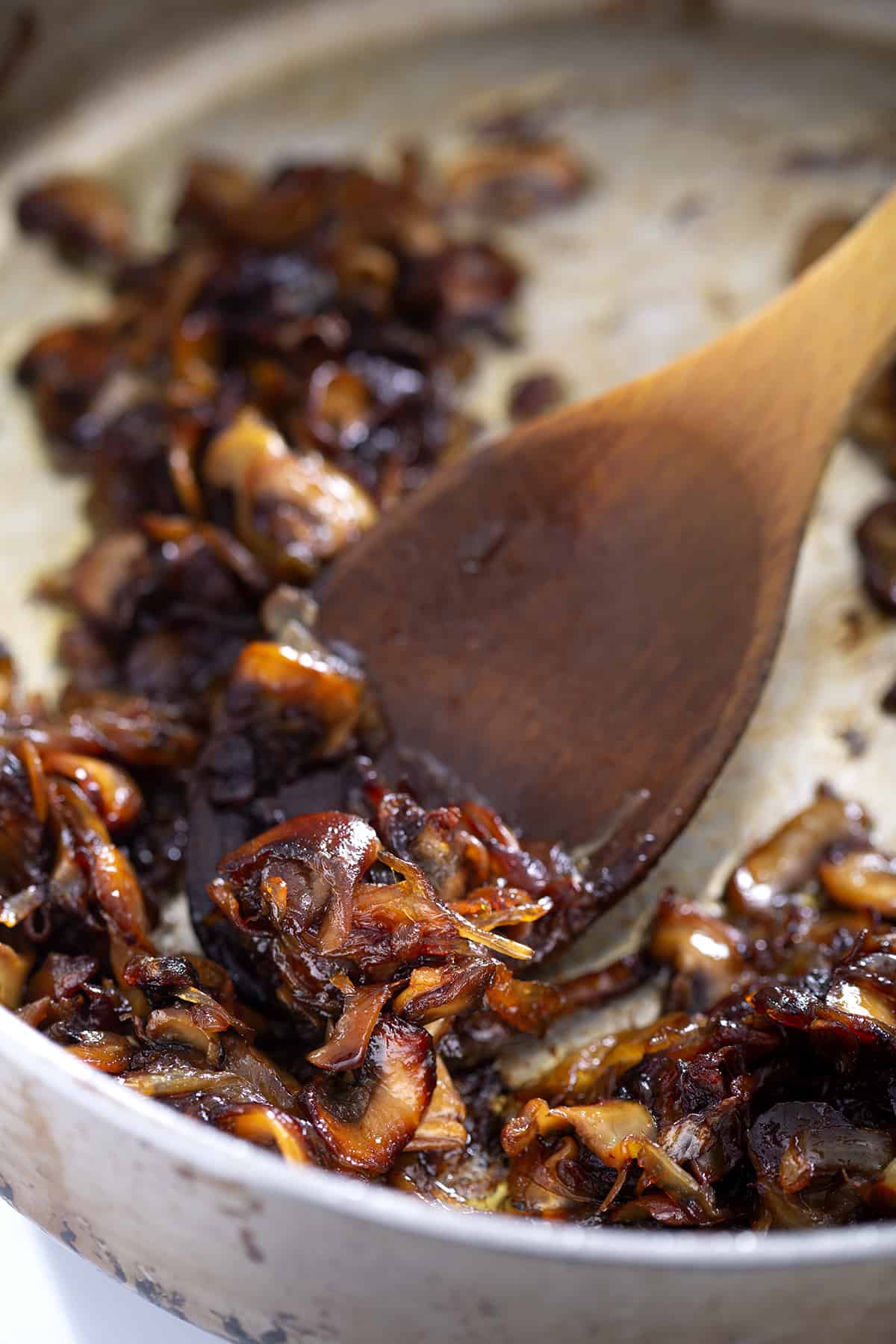 wooden spoonful of caramelized onions and mushrooms in pan