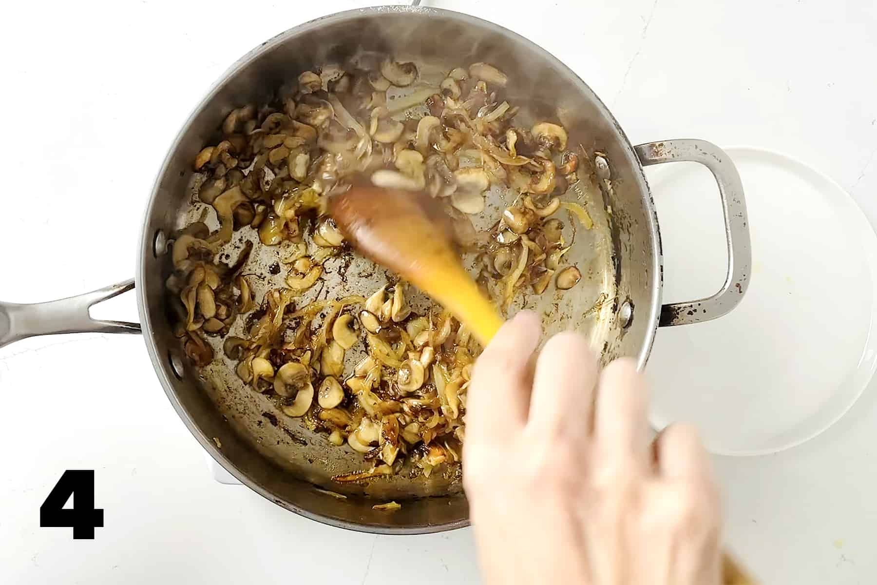 wooden spoon stirring onions and mushrooms in frying pan