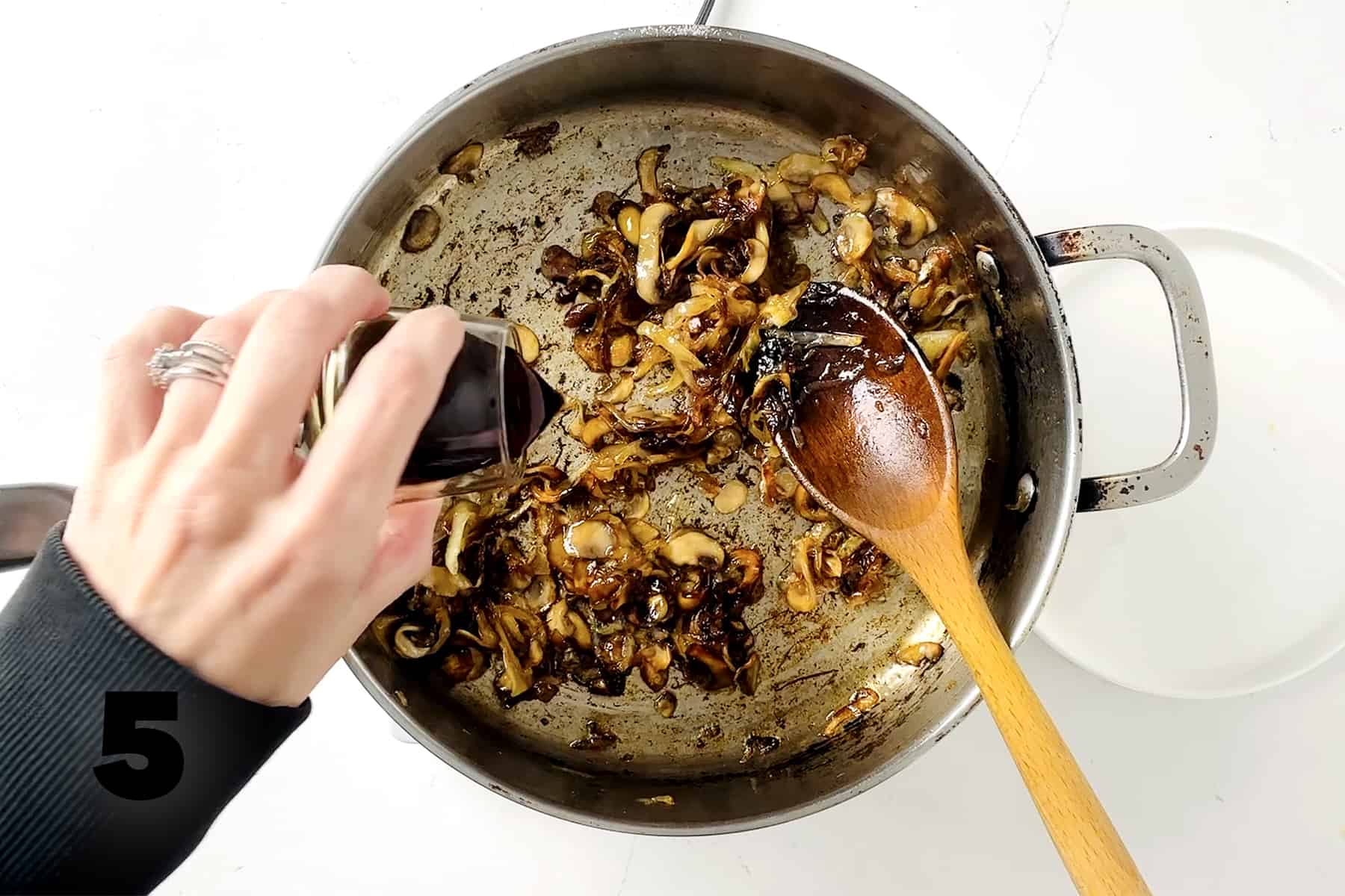 pouring balsamic vinegar into frying pan with onions and mushrooms
