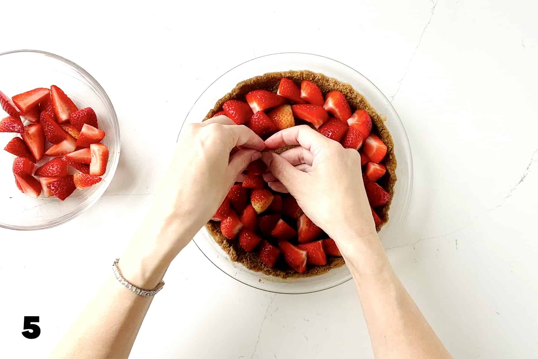 hands placing strawberries in graham cracker crust