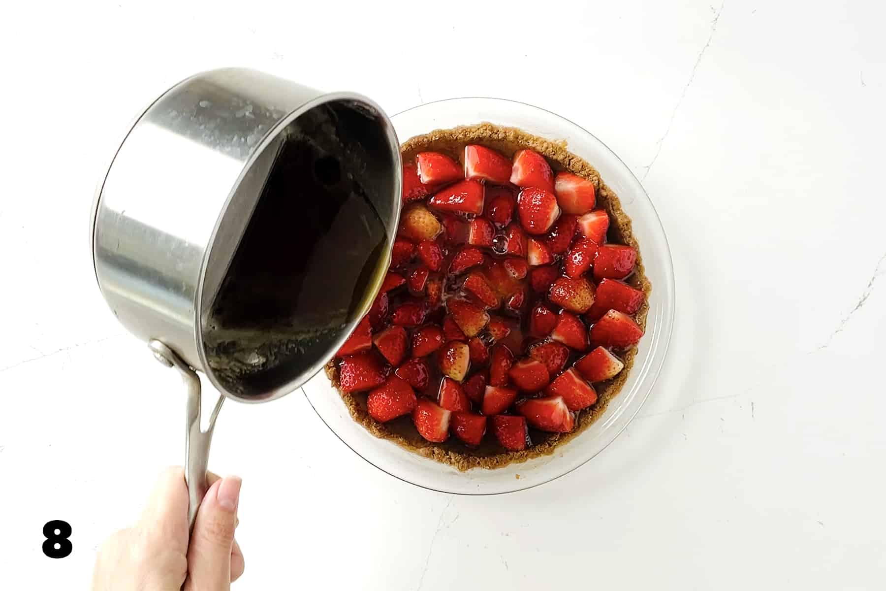 pouring honey syrup into strawberry lined graham cracker crust