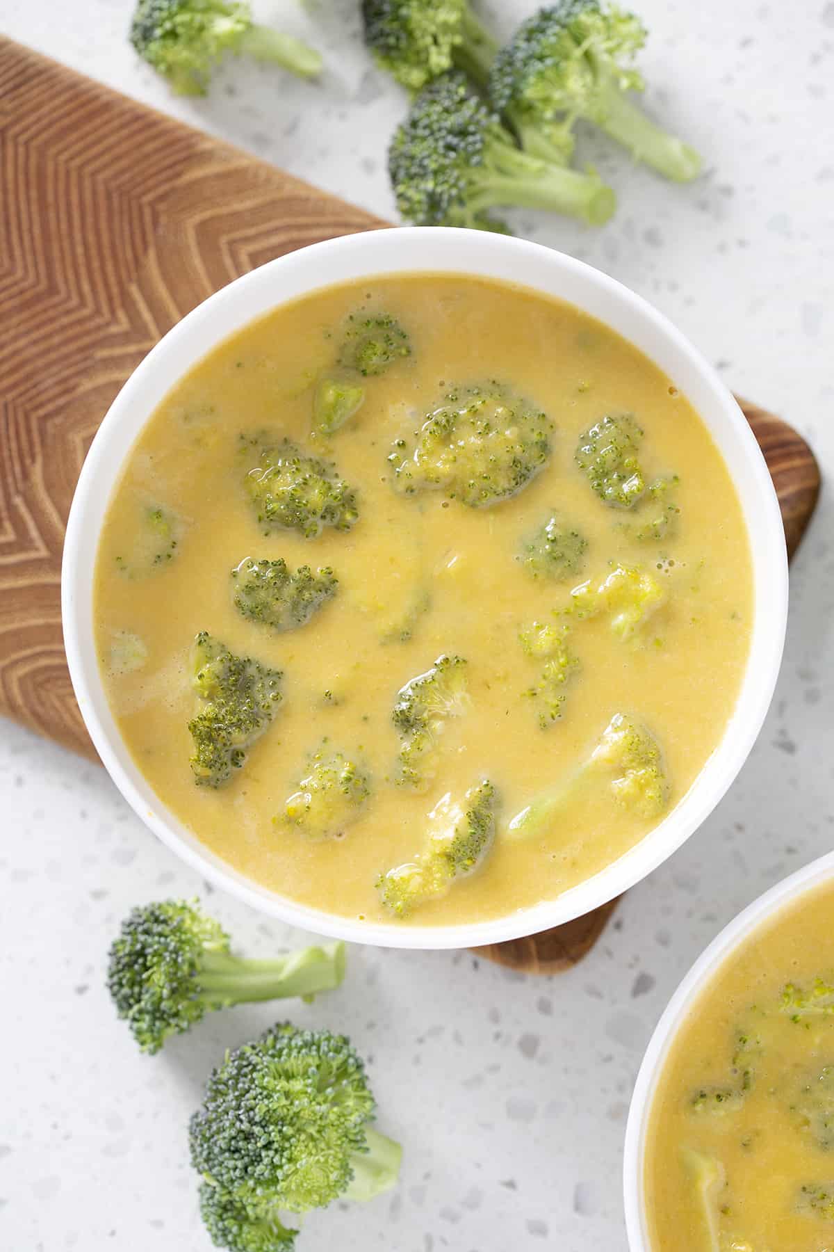 bowls of vegan broccoli cheddar soup surrounded by broccoli florets
