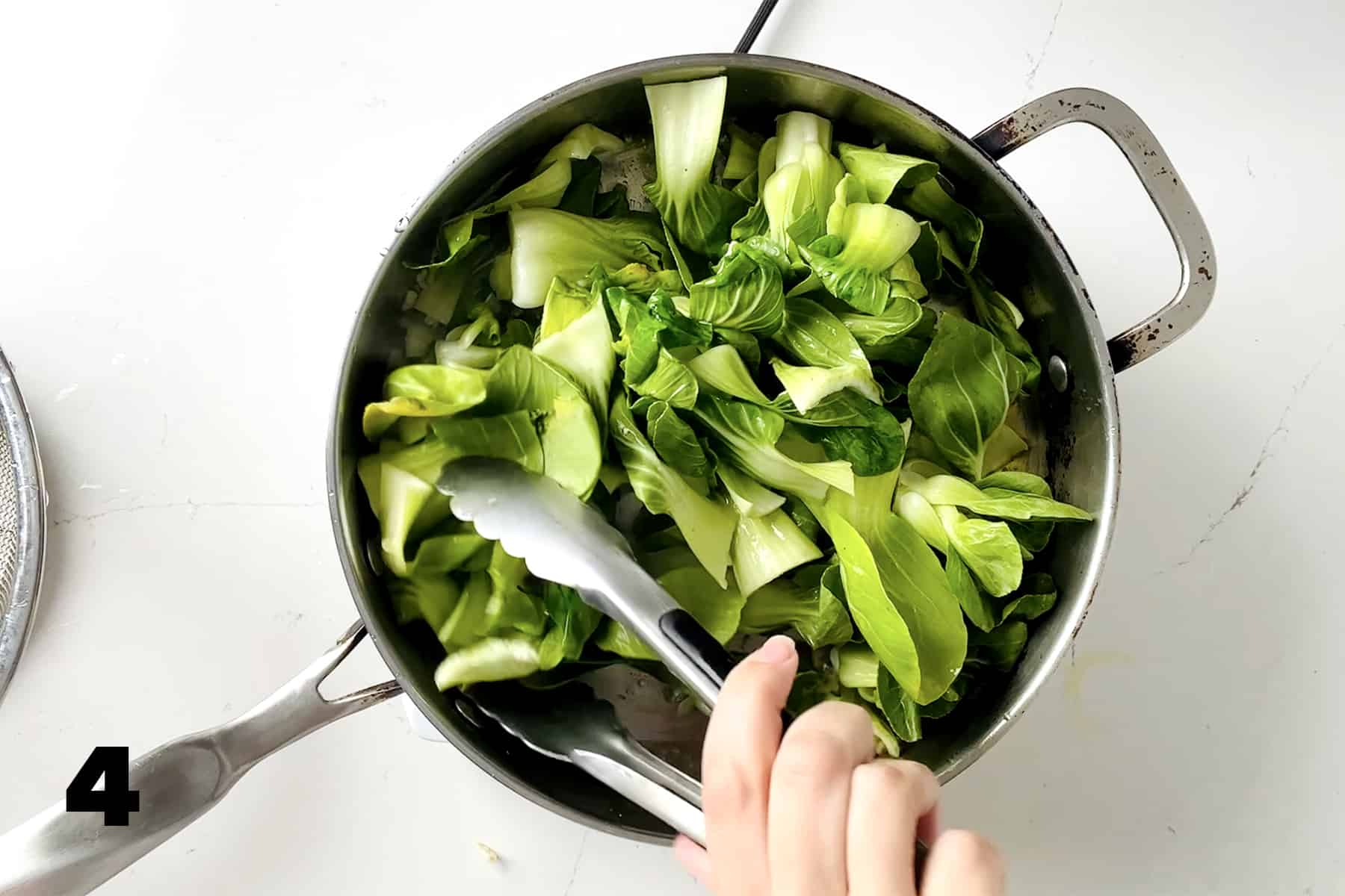 tossing shanghai bok choy with tongs in pan