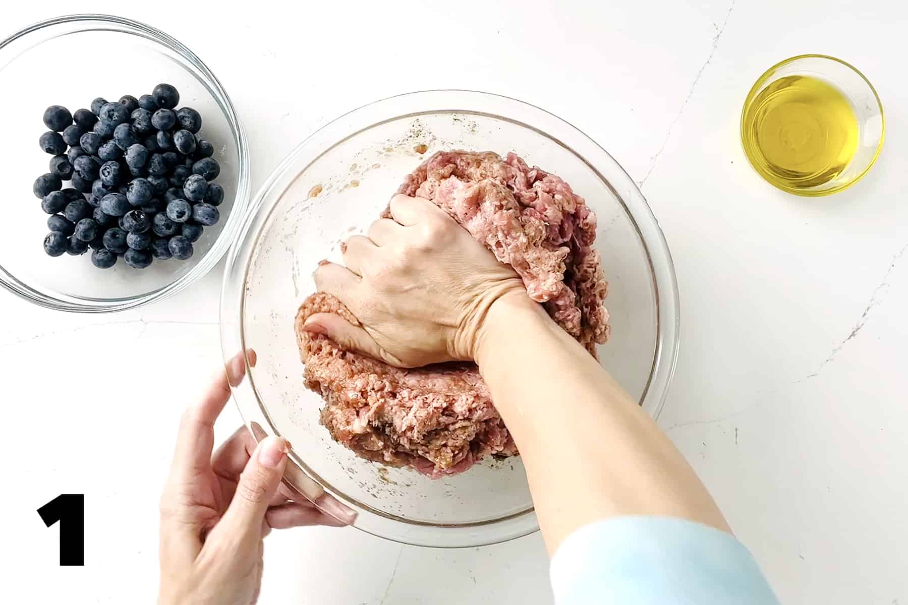 hand mixing ground meat with bowl of blueberries and oil