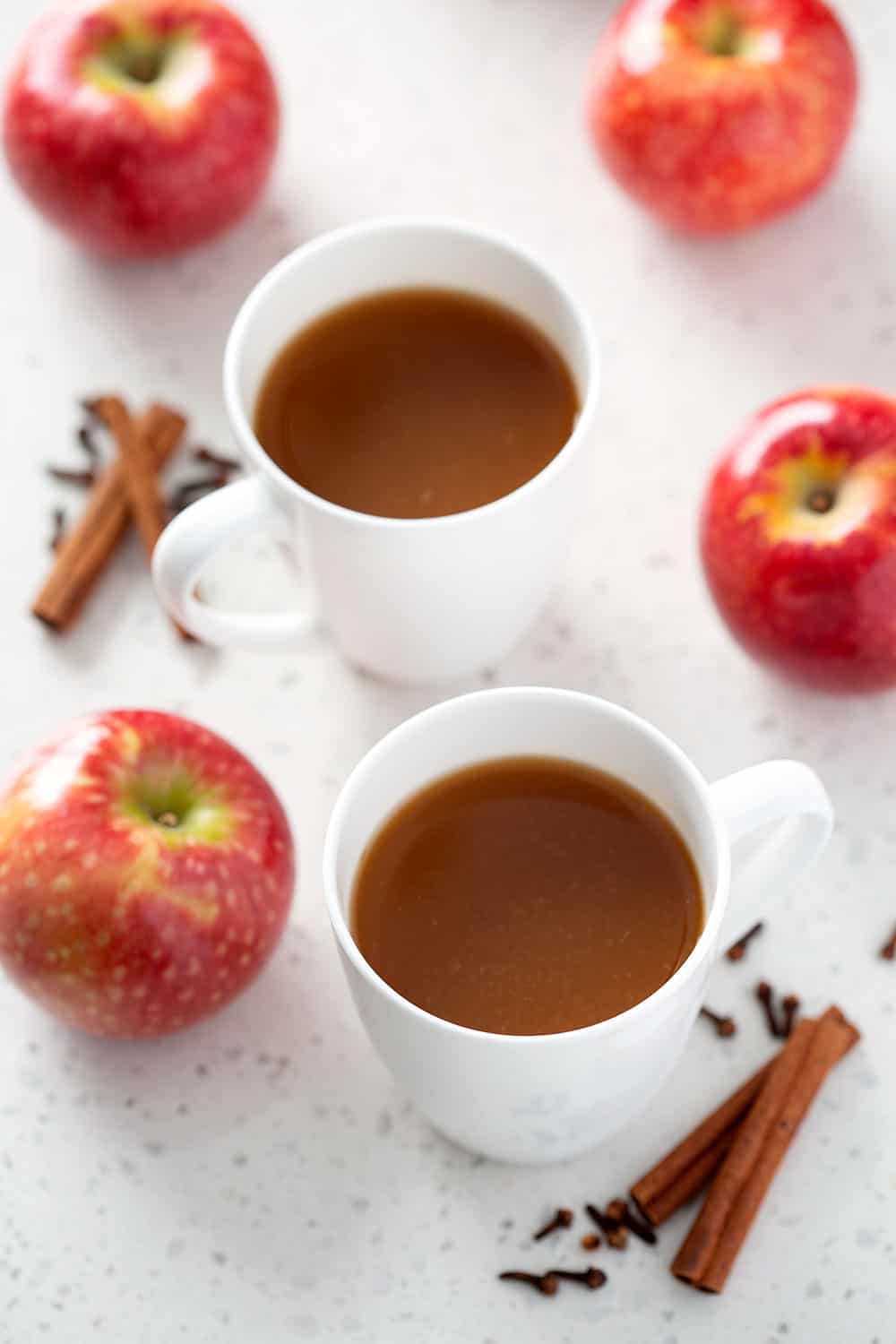 mugs of instant pot apple cider with apples and spices