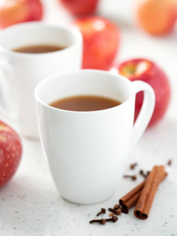 mugs of instant pot apple cider with apples and spices