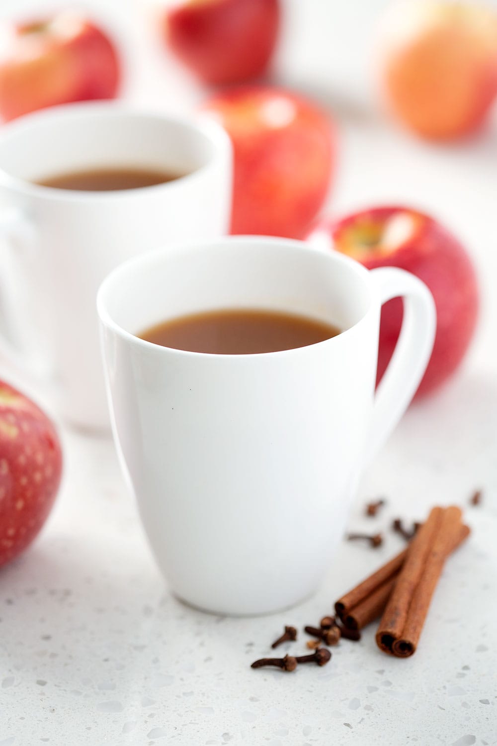 mugs of apple cider with apples and spices in the background