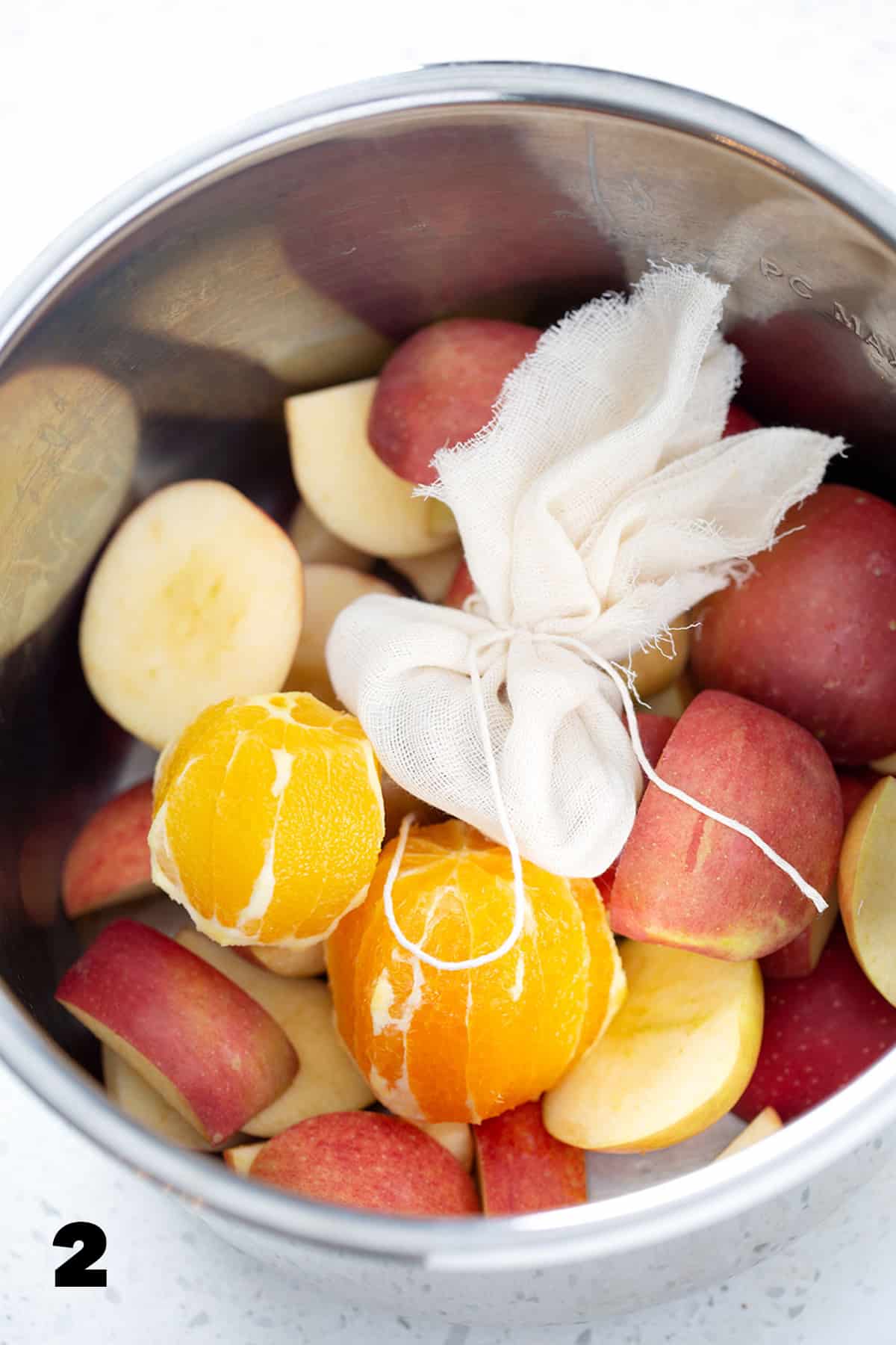Instant pot full of oranges, apples and cheesecloth sachet.