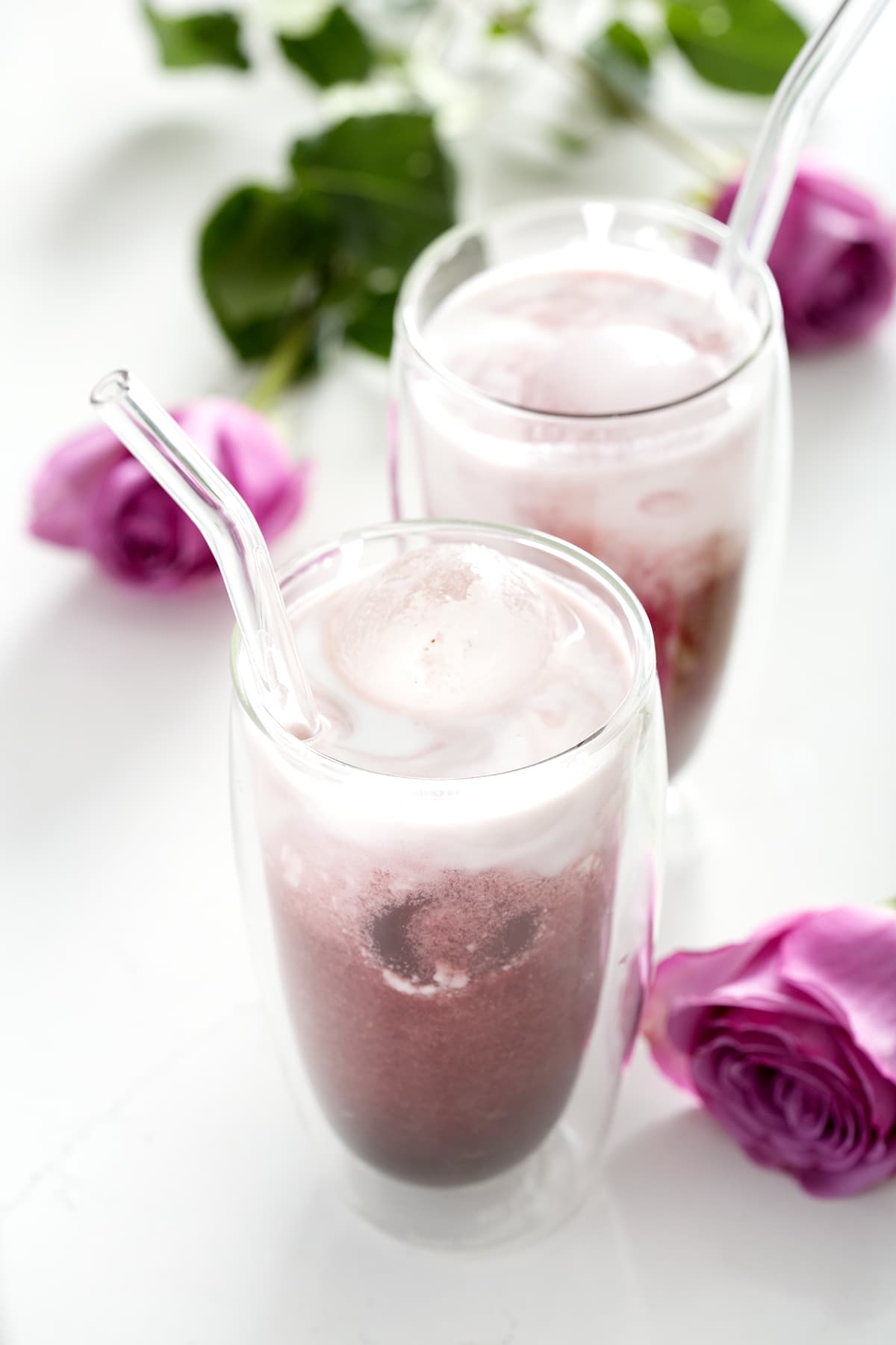 glass of iced rose latte with glass straw and pink roses