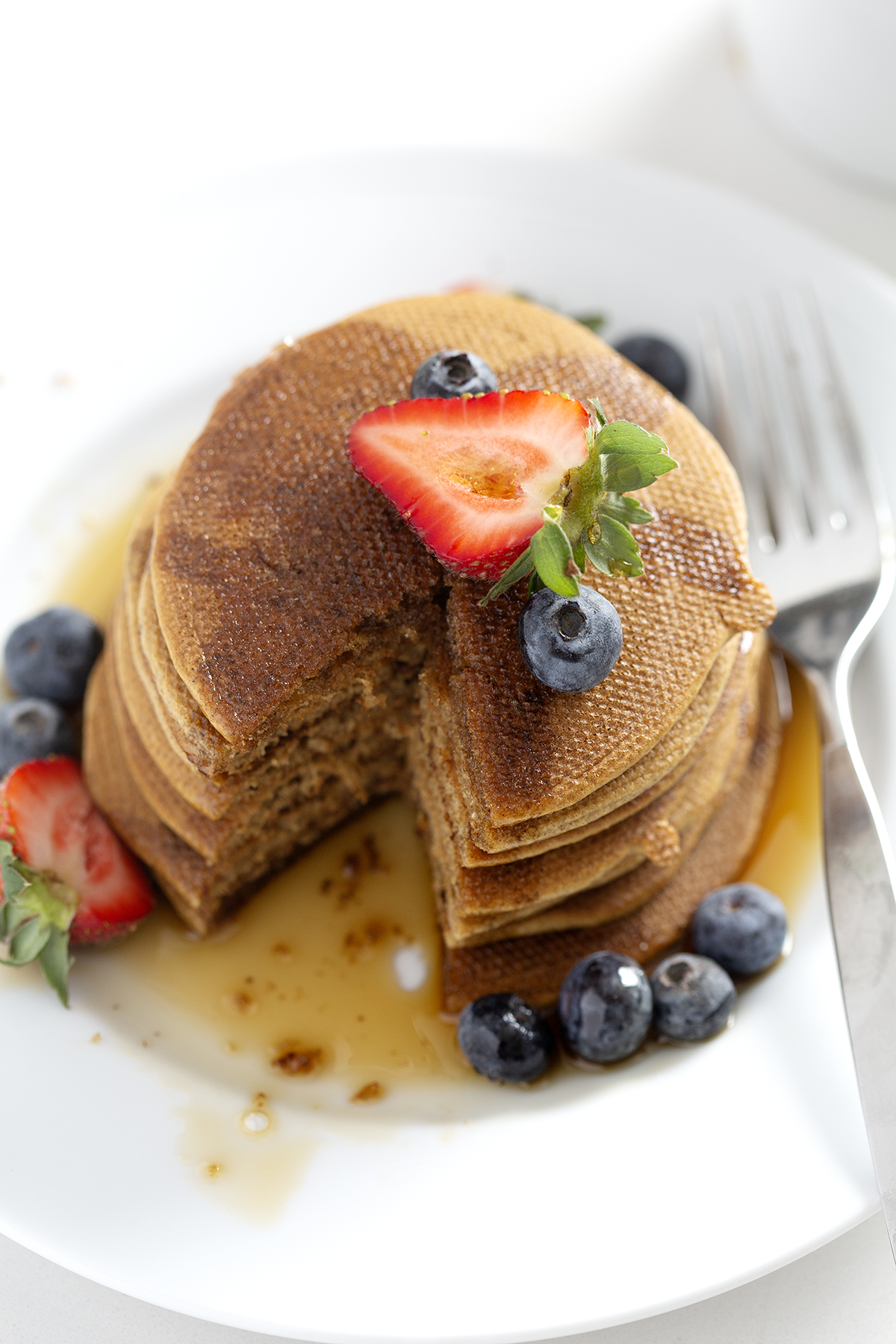 stack of pancakes covered in berries and maple syrup