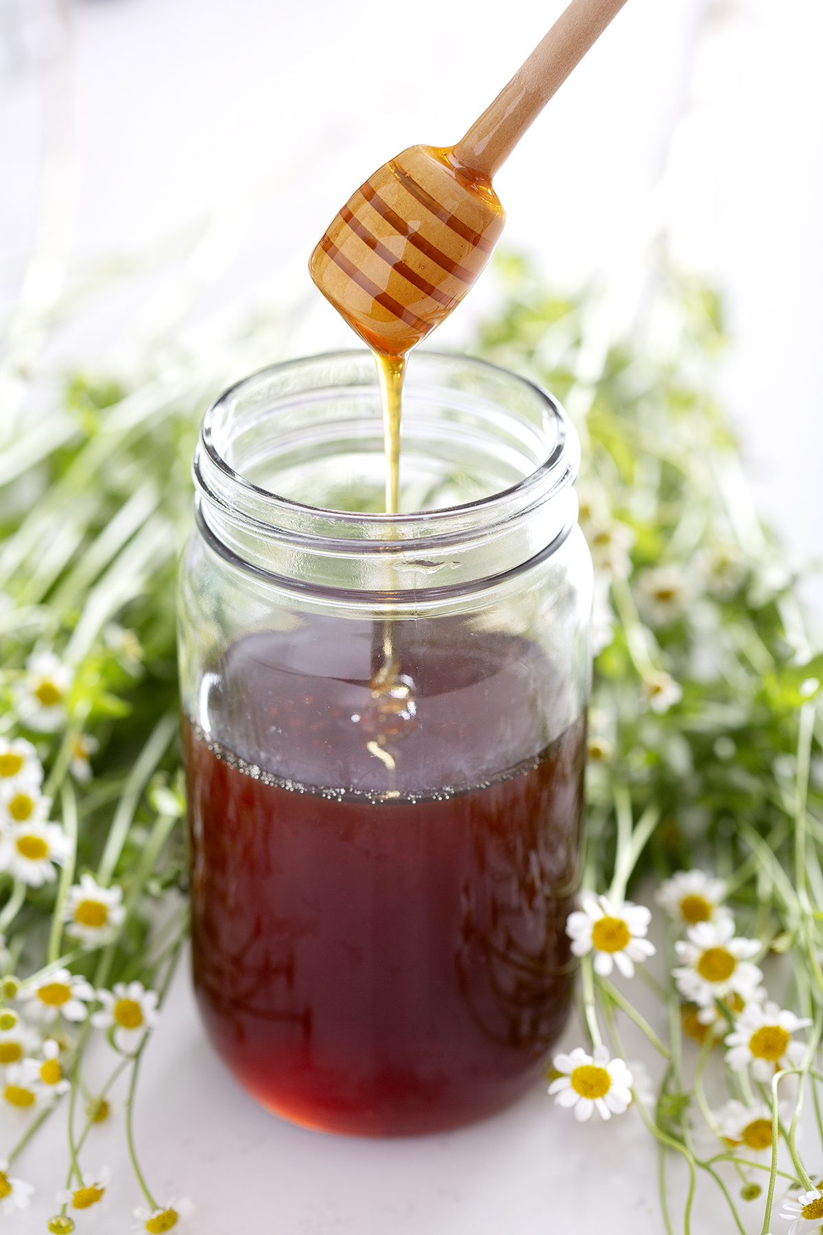 honey dipper drizzling honey into jar of honey with flowers
