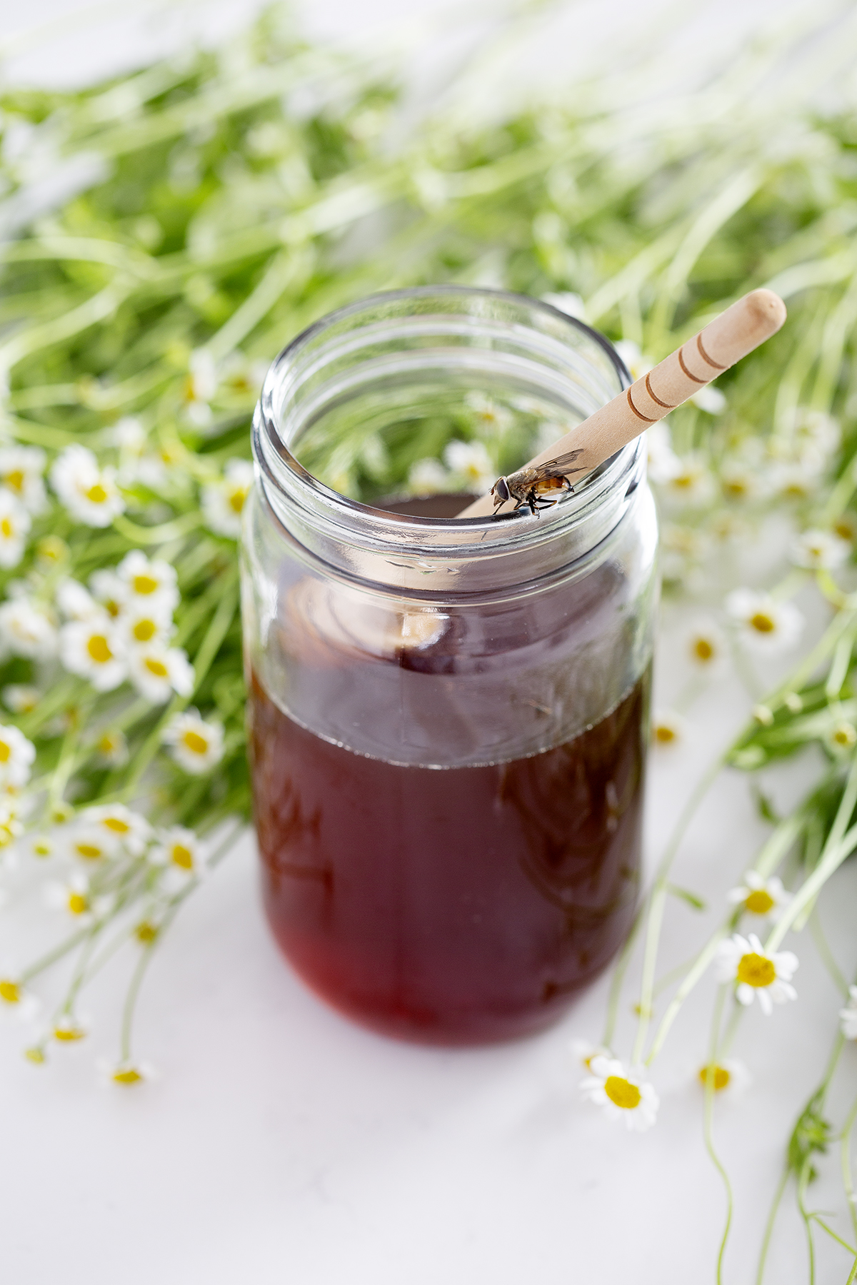 jar of honey with dipper, bee and surrounded by flowers