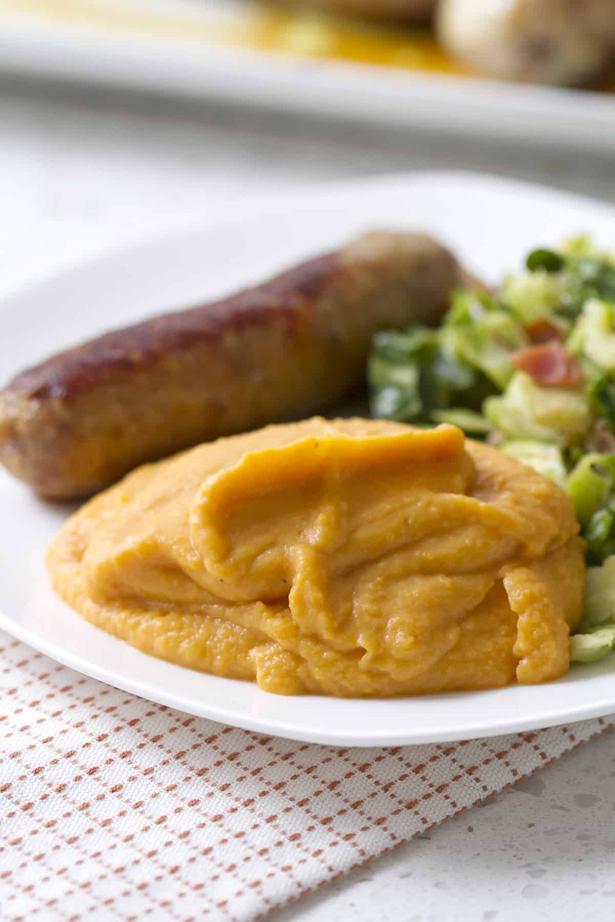 mashed sweet potatoes on plate with sausage and brussel sproouts