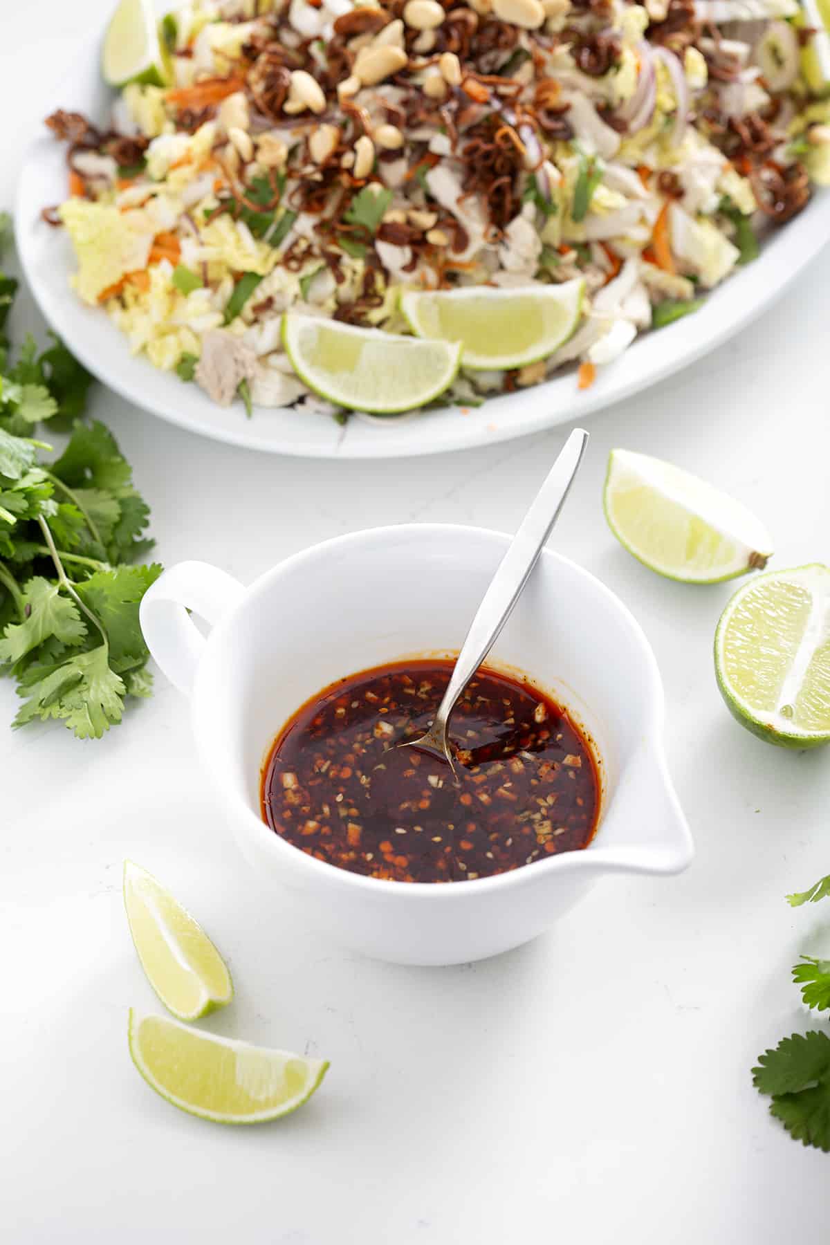 small bowl of nuoc mam surrounded by limes, cilantro and goi ga