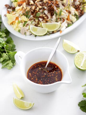 small bowl of nuoc mam surrounded by lime, cilantro and goi ga