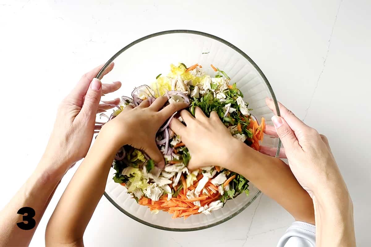 kids hands mixing salad while adult hands hold large bowl