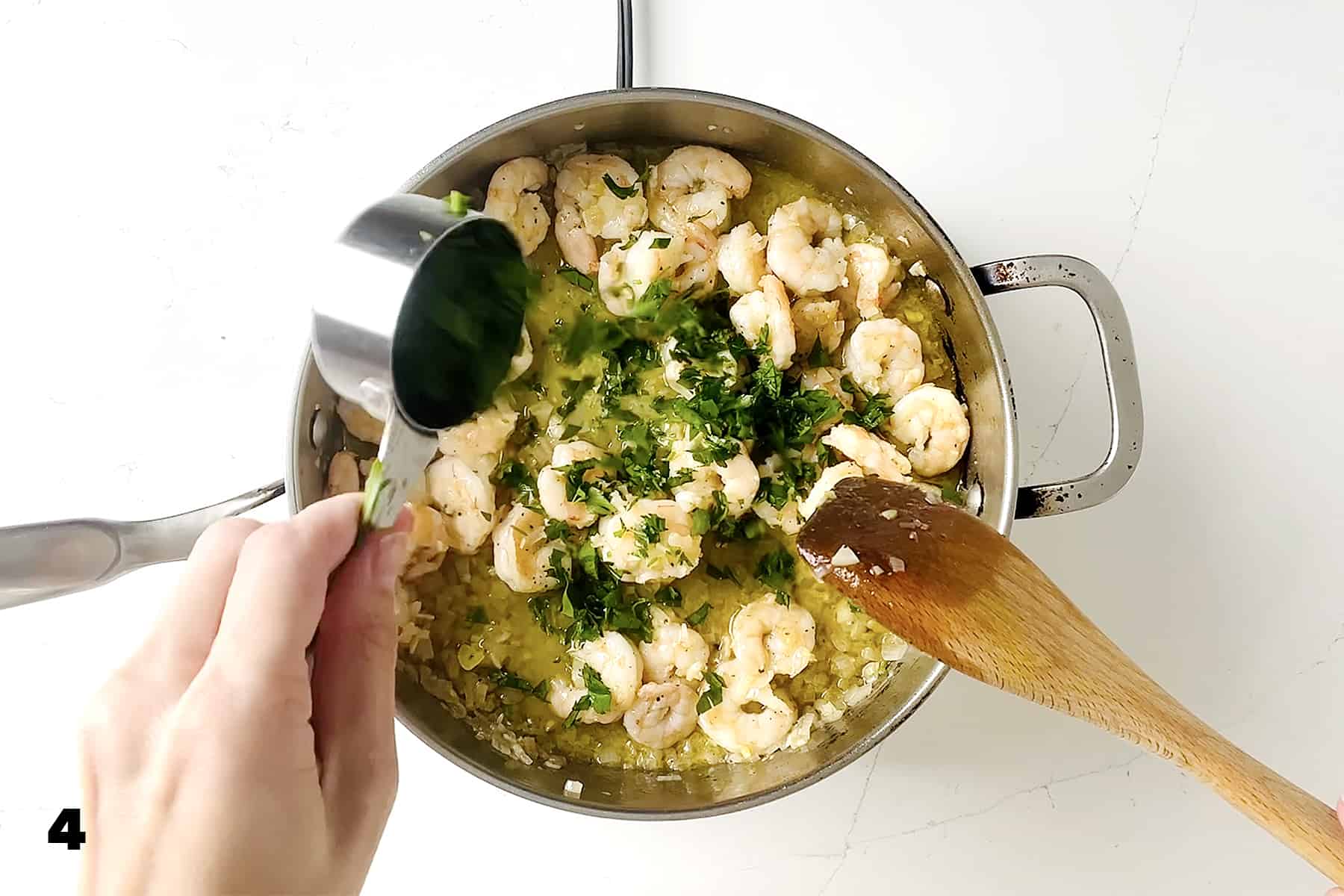 adding parsley to shrimp in a pan with wooden spoon