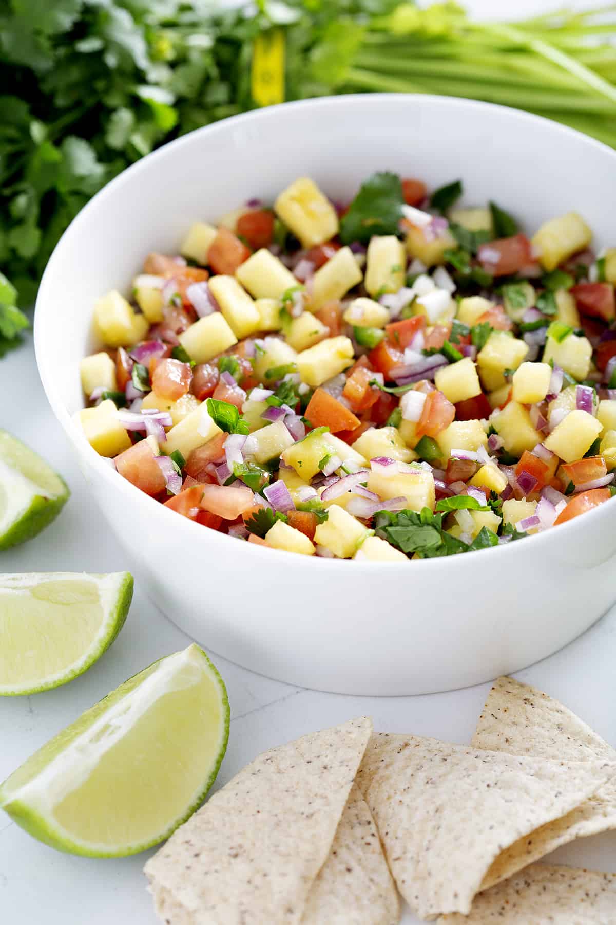 bowl of pineapple pico de gallo surrounded by cilantro, lime, tortilla chips