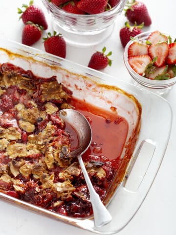 pan of gluten free strawberry rhubarb crumble with serving spoon and strawberries