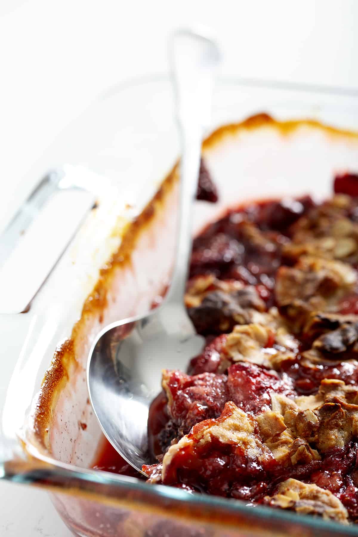 serving spoon in glass pan of strawberry rhubarb crumble