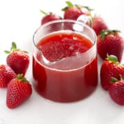 small pitcher of Strawberry Rhubarb Syrup surrounded by strawberries