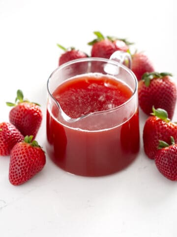 small pitcher of Strawberry Rhubarb Syrup surrounded by strawberries