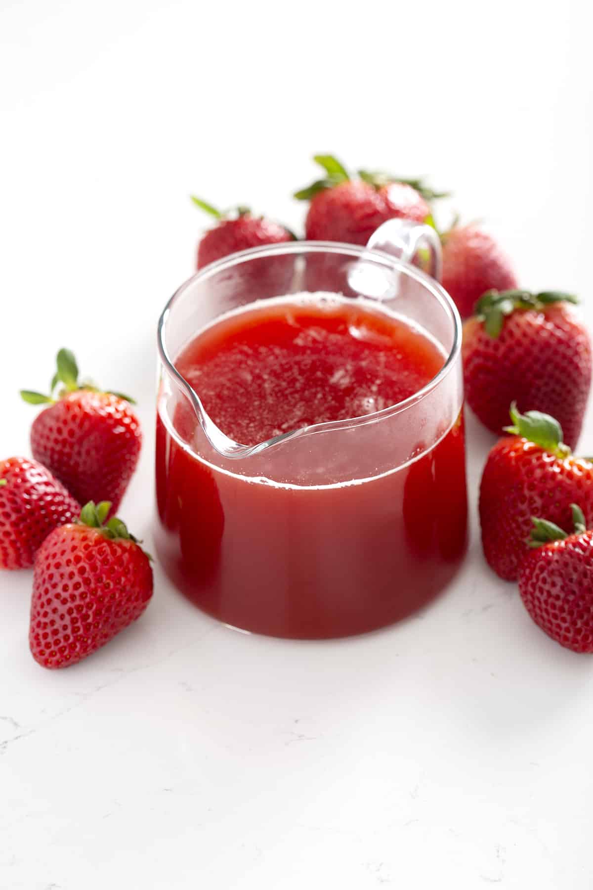 small pitcher of fruit flavor simple syrup surrounded by strawberries