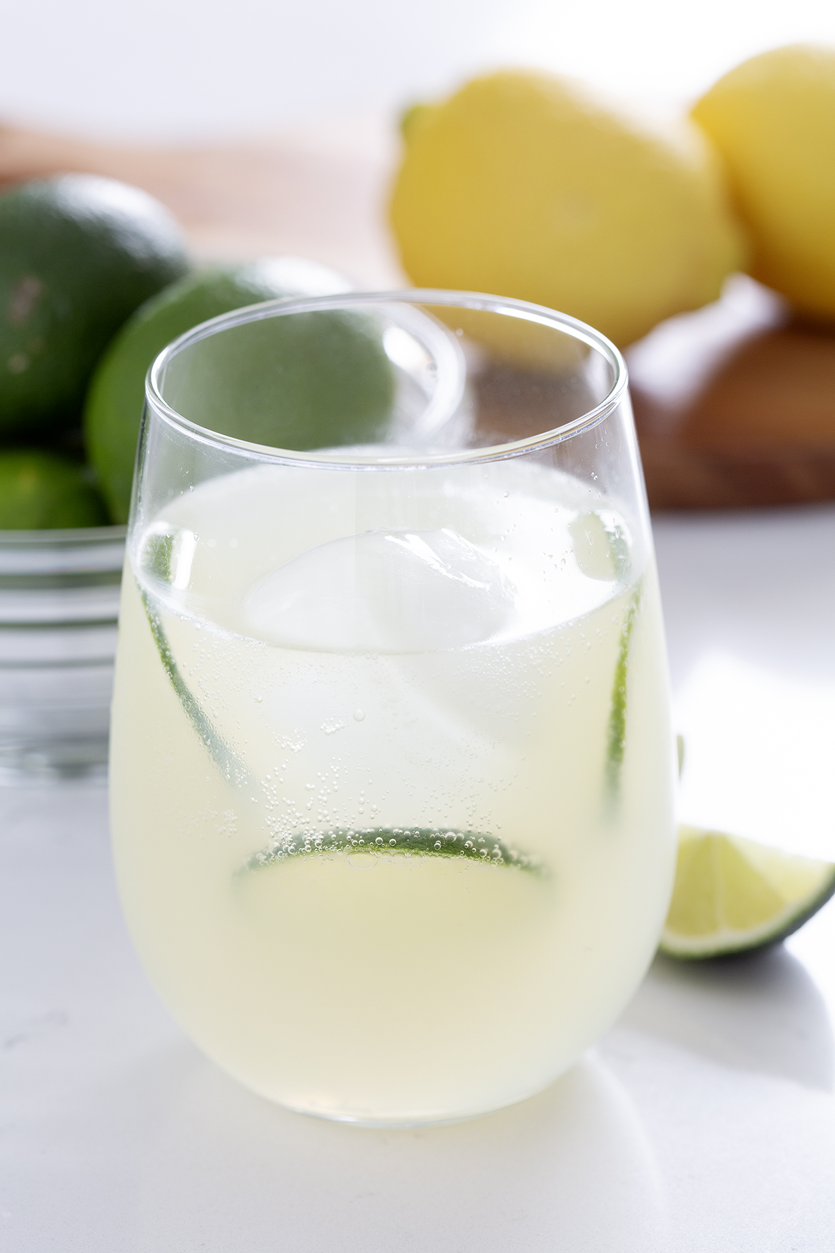 Stemless wine glass filled with gin rickey surrounded by lemons and limes