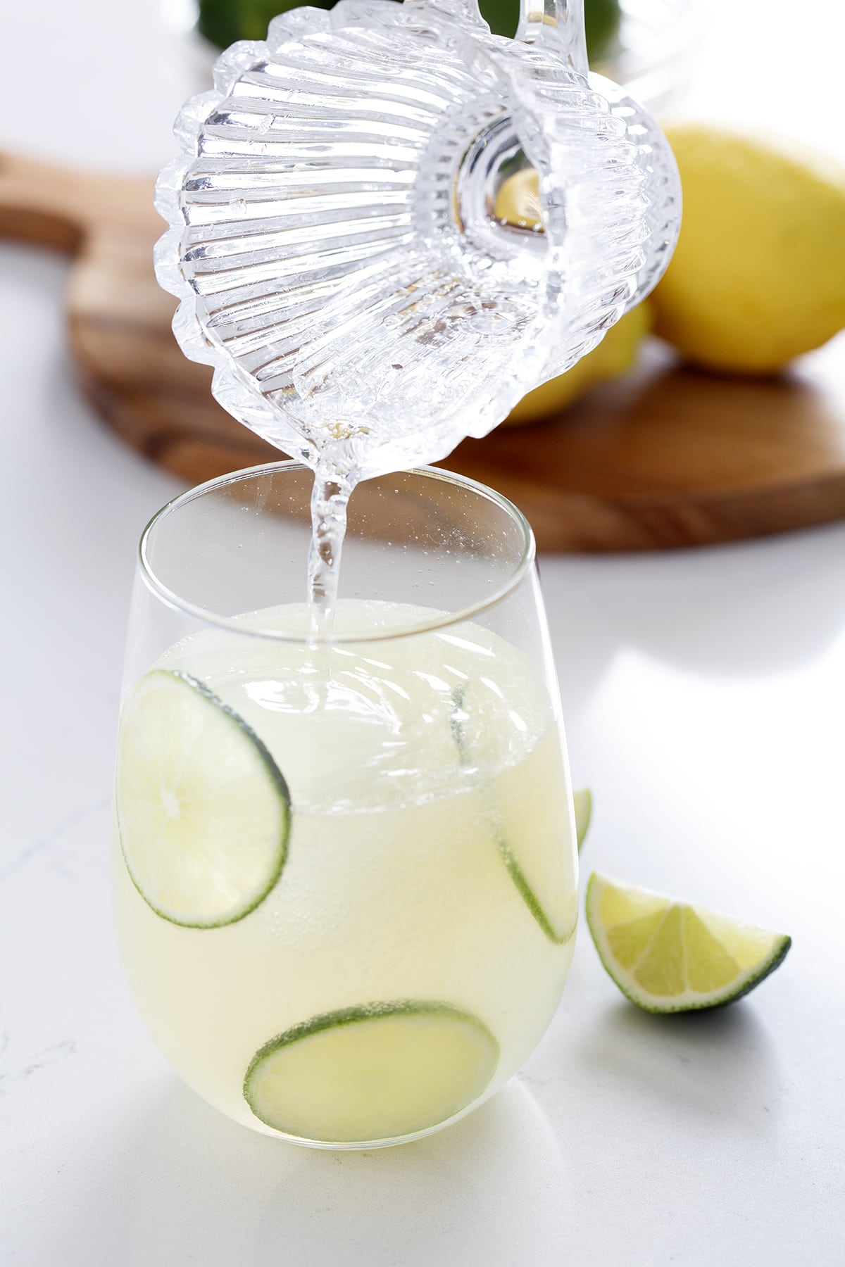 pouring sparkling water into gin rickey with limes