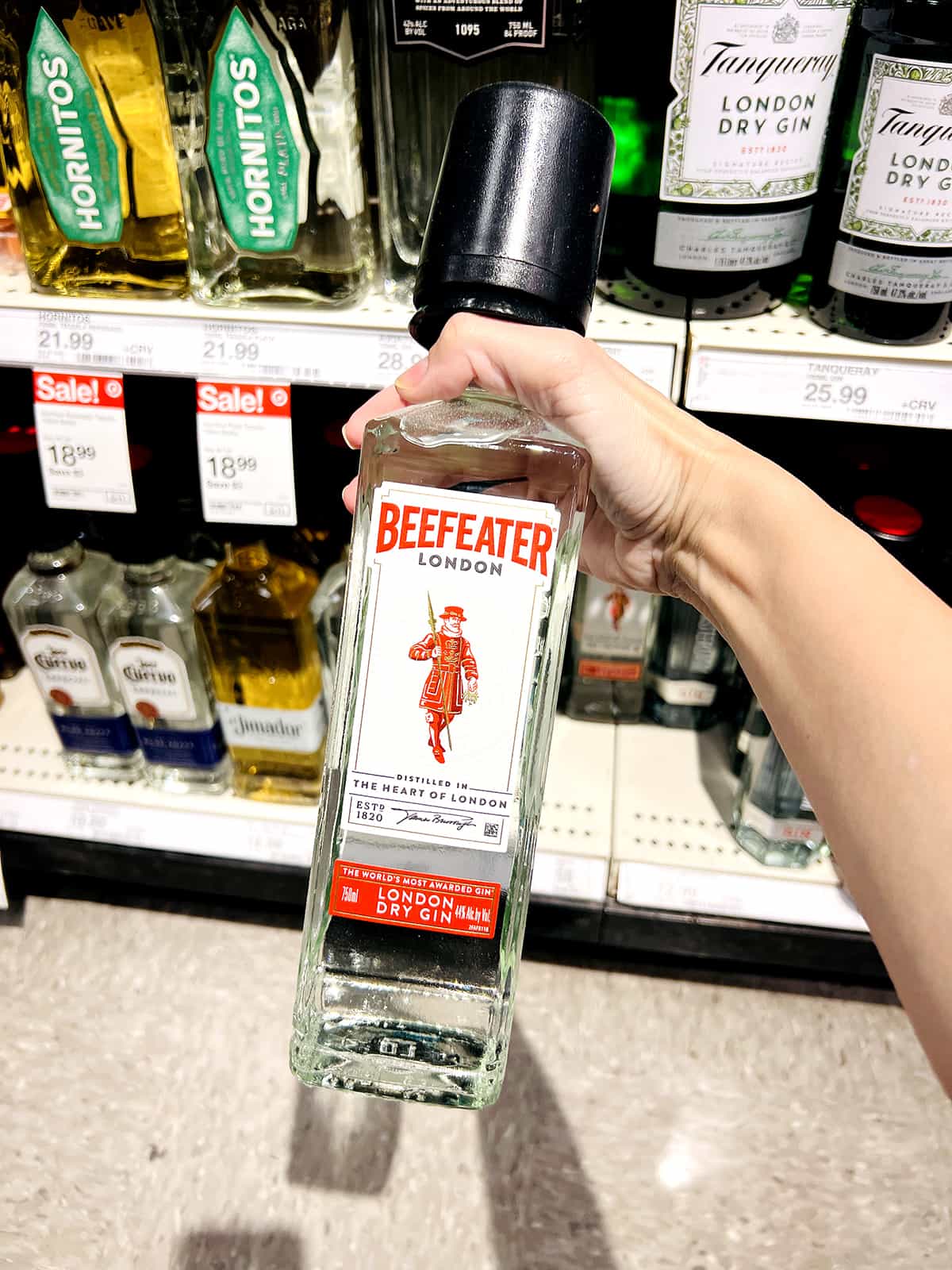 hand holding bottle of beefeater gin in grocery store aisle