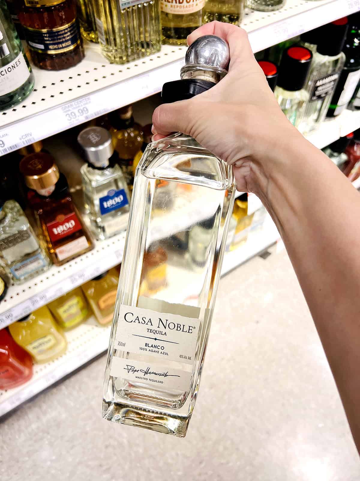 hand holding casa noble tequila bottle in grocery store aisle