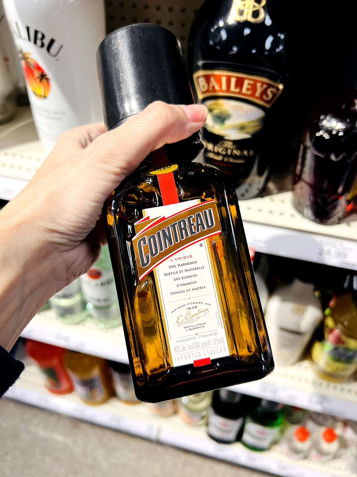hand holding bottle of cointreau in grocery store aisle