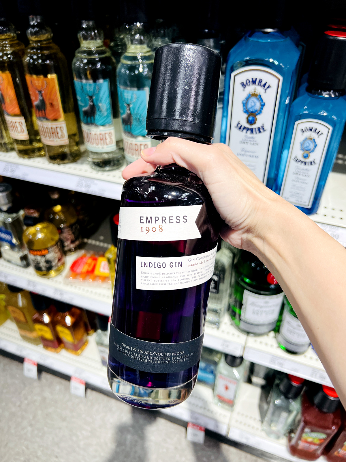 hand holding bottle of empress gin in grocery store aisle