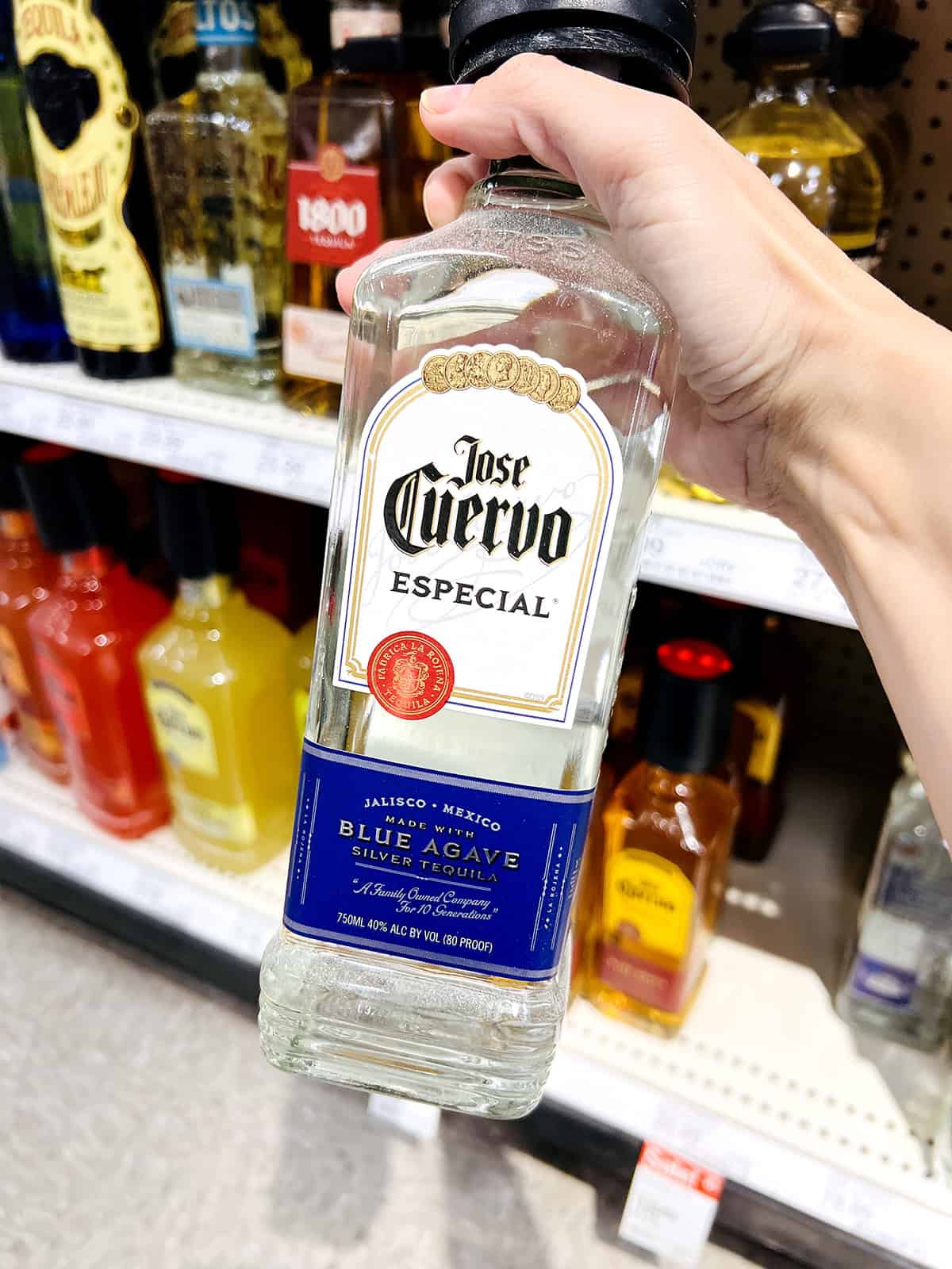 hand holding jose cuervo tequila bottle in grocery store aisle