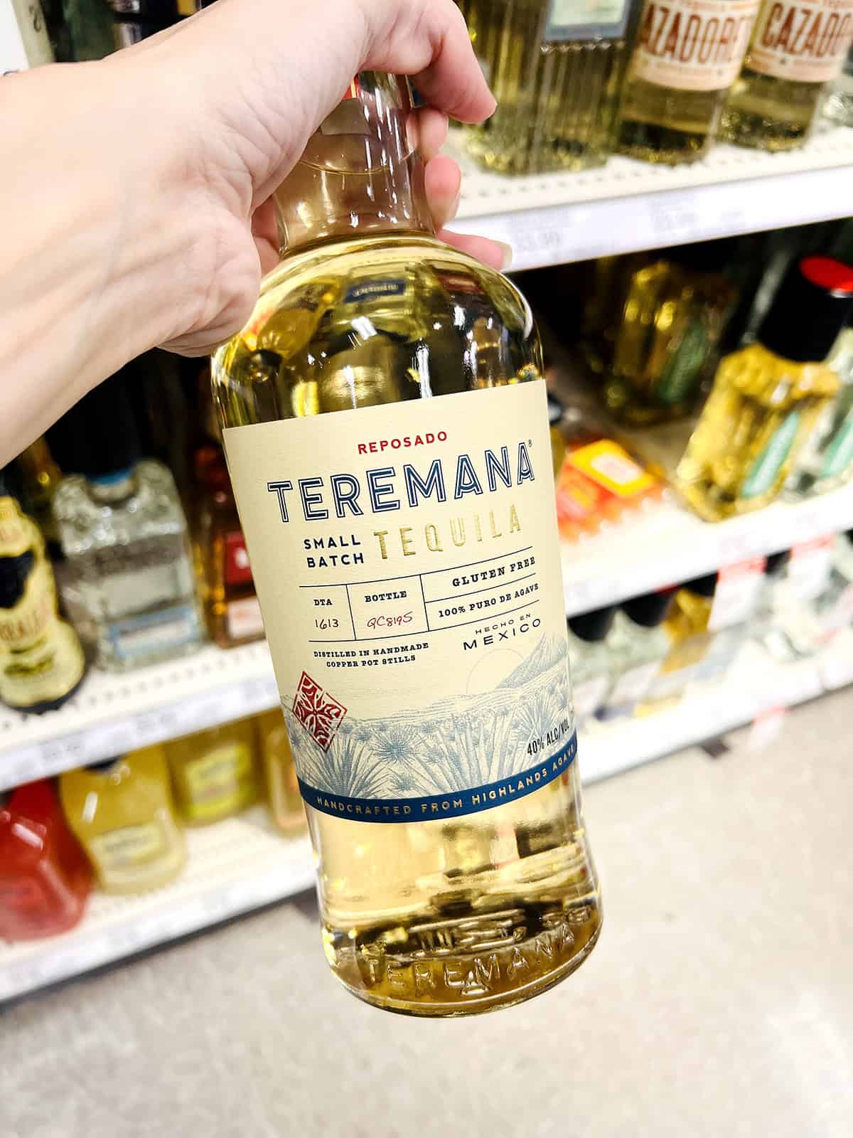 hand holding bottle of teremana tequila in grocery store aisle