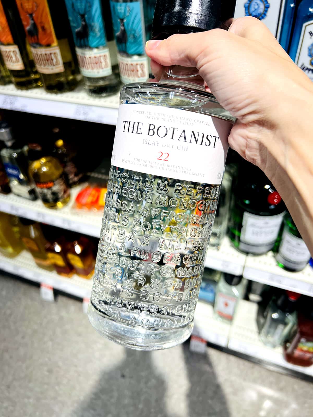 hand holding bottle of the botanist gin in grocery store aisle