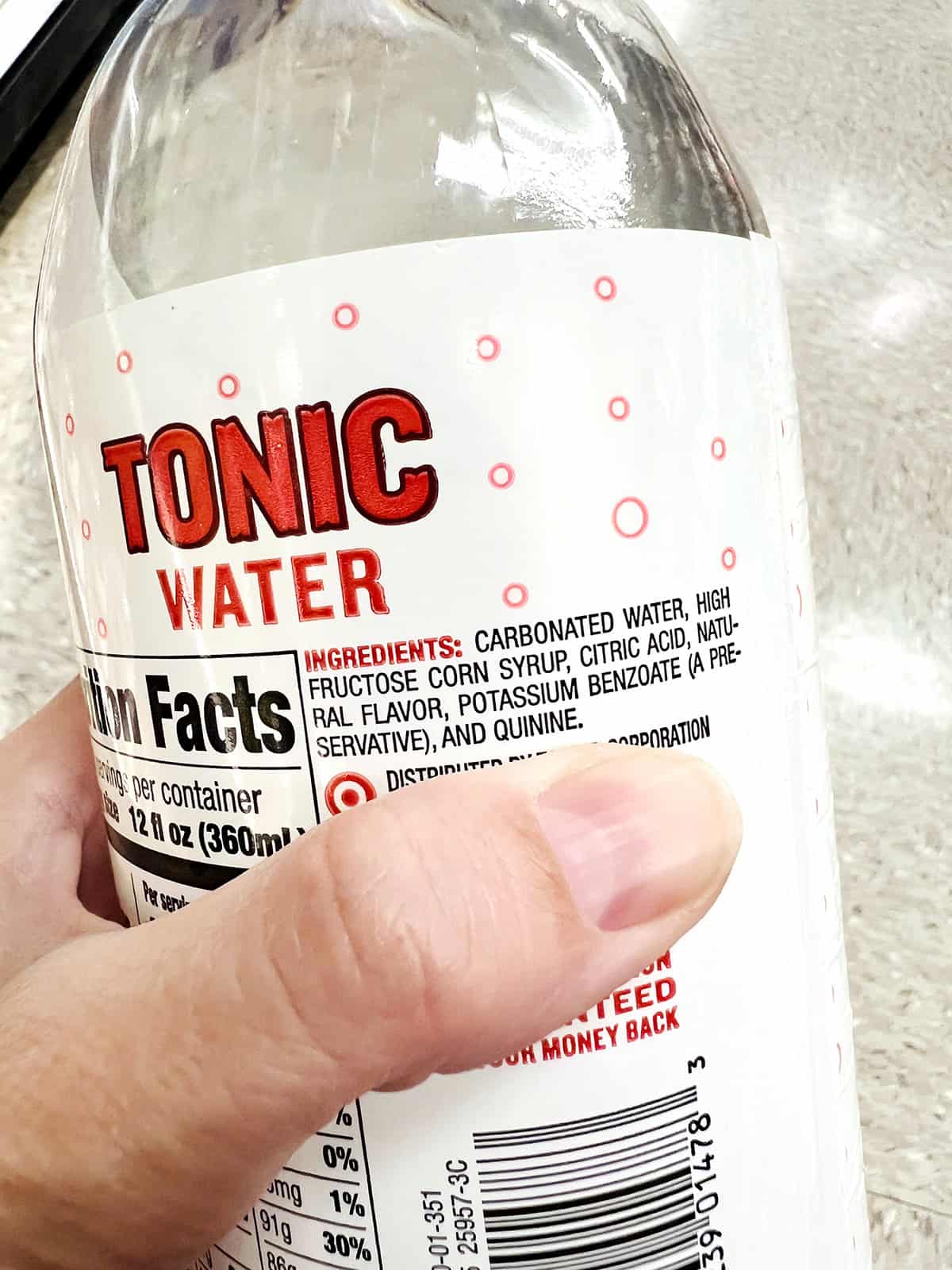 hand holding bottle of tonic water with close up of ingredients
