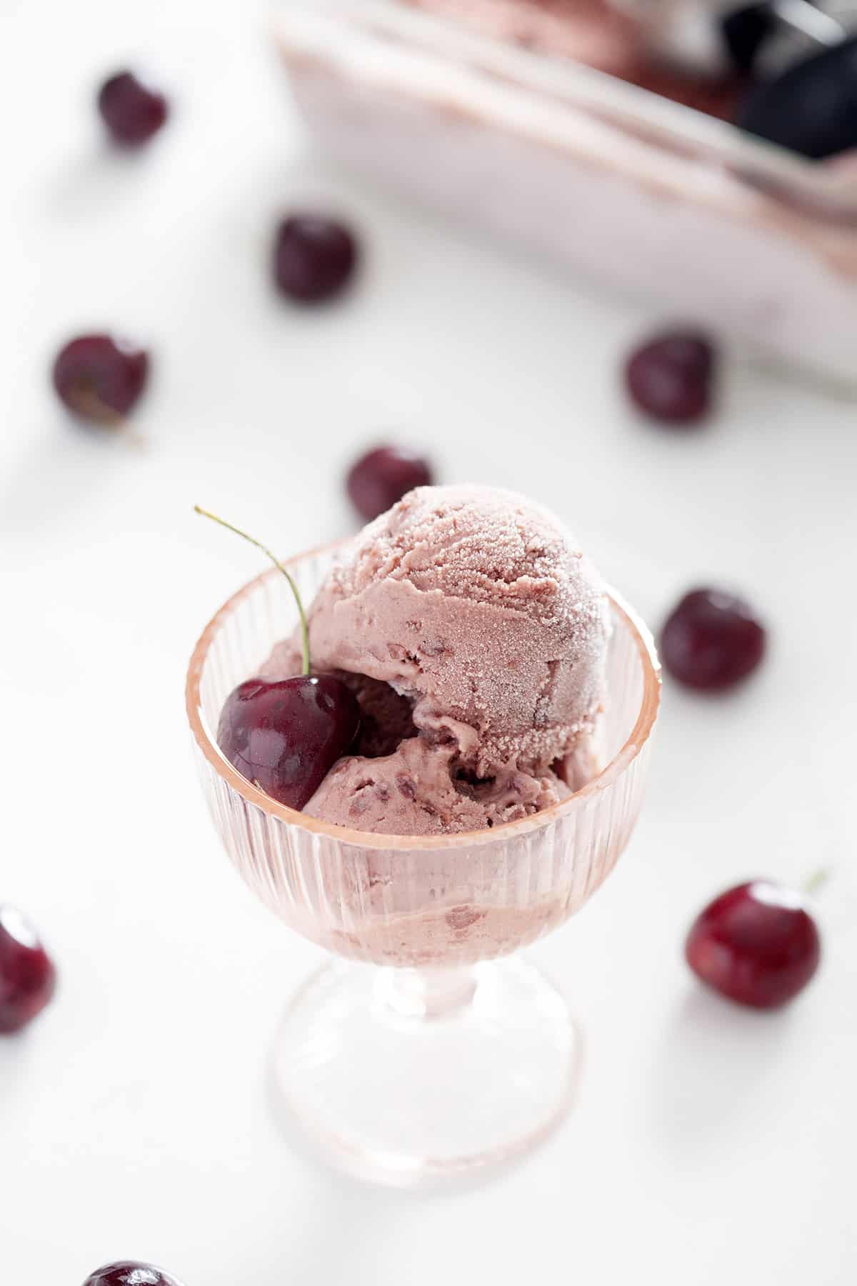 pink glass cup with AIP ice cream with cherry surrounded by cherries