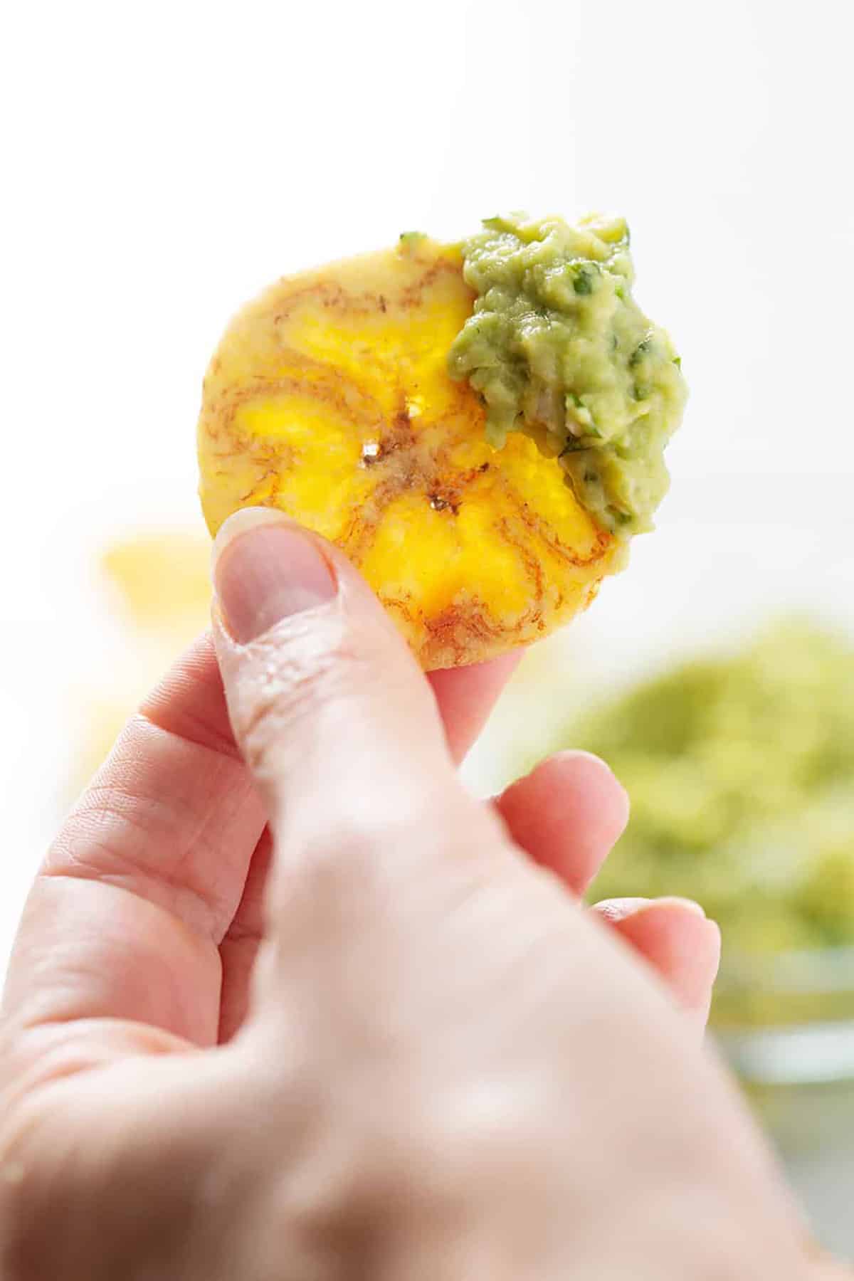 hand holding plantain chip with guacamole