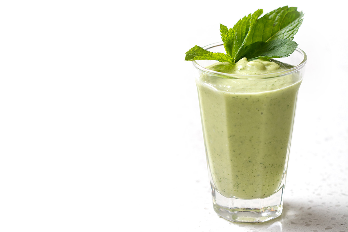 green smoothie with mint sprig as garnish on white background